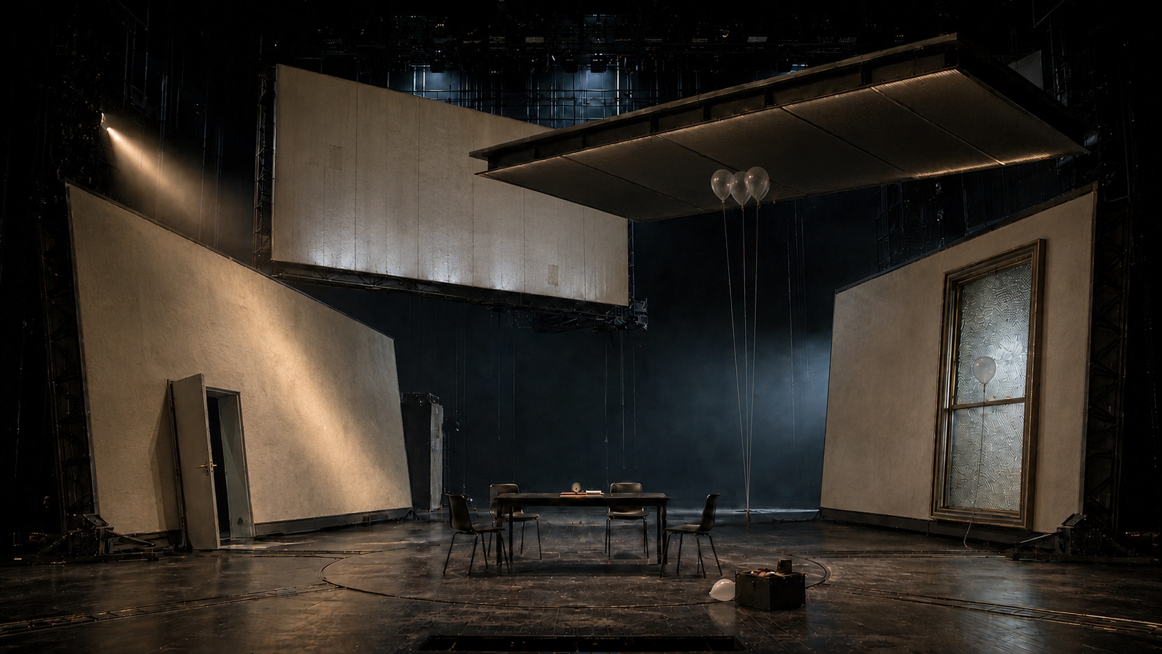 Empty stage for The Story Of Simple: four translucent room shells, a table and four chairs, an open dark door, a sealed window and clear balloons caught overhead.